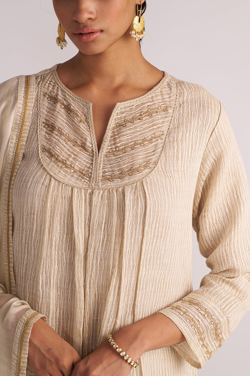 Close-up of a person wearing a Beige Woven Kurta Set traditional outfit with gold accents.
